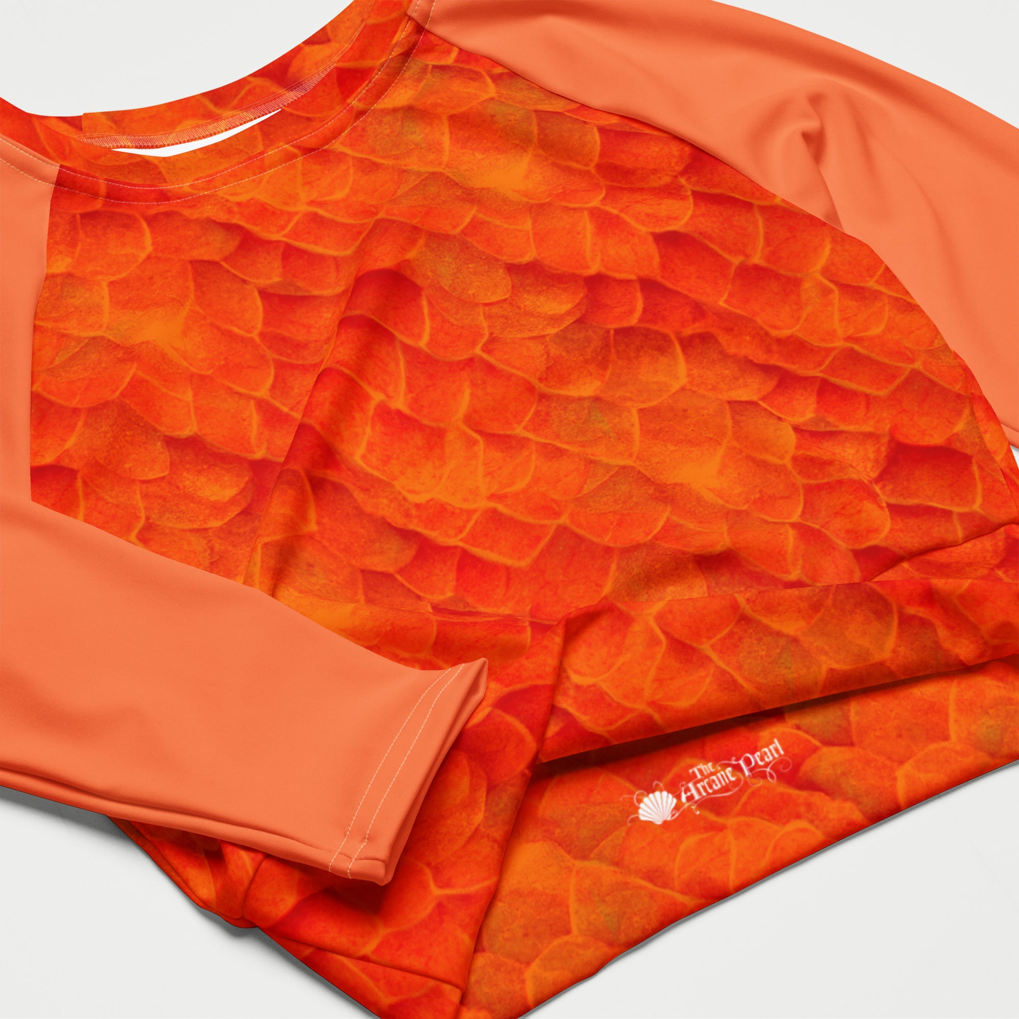 A close-up of a long-sleeve athletic top with a textured orange  scale-like pattern on the front and solid coral-orange sleeves and collar. 